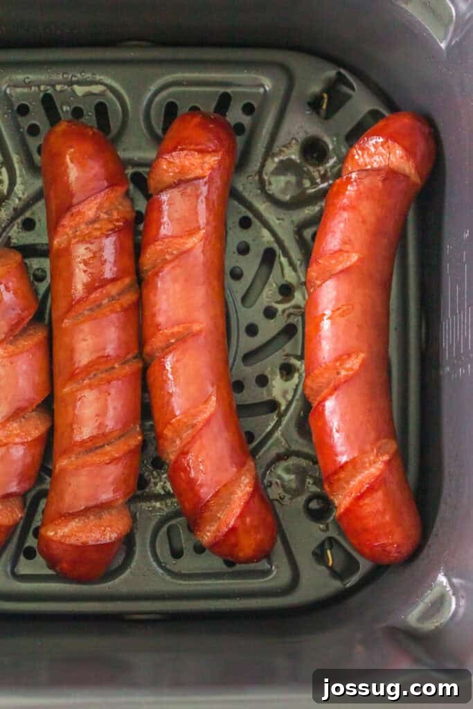 Hot dogs halfway cooked, skin starting to crisp inside air fryer