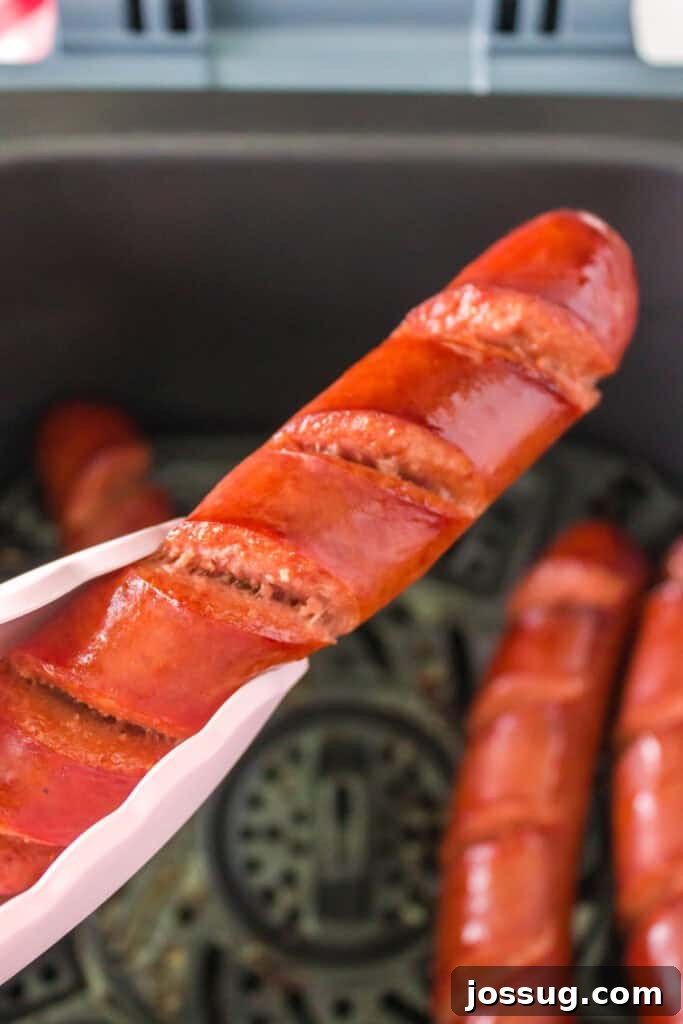 Tongs lifting a fully cooked scored hot dog from the air fryer