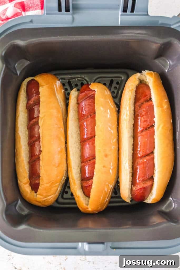 Three hot dogs placed in buns inside the air fryer ready to be toasted