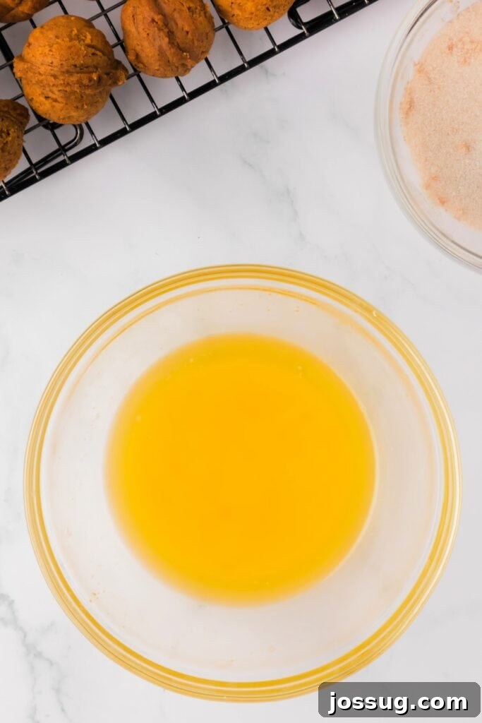 Pumpkin Poppers 10 Melted butter in a glass bowl next to baked pumpkin donut holes and a bowl of cinnamon sugar.