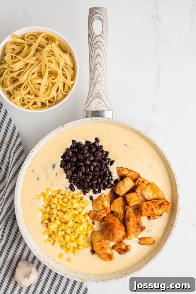 Fiesta Chicken Fettuccine Alfredo 12 Cooked chicken, black beans, and corn added to the creamy sauce in the skillet, being mixed thoroughly.