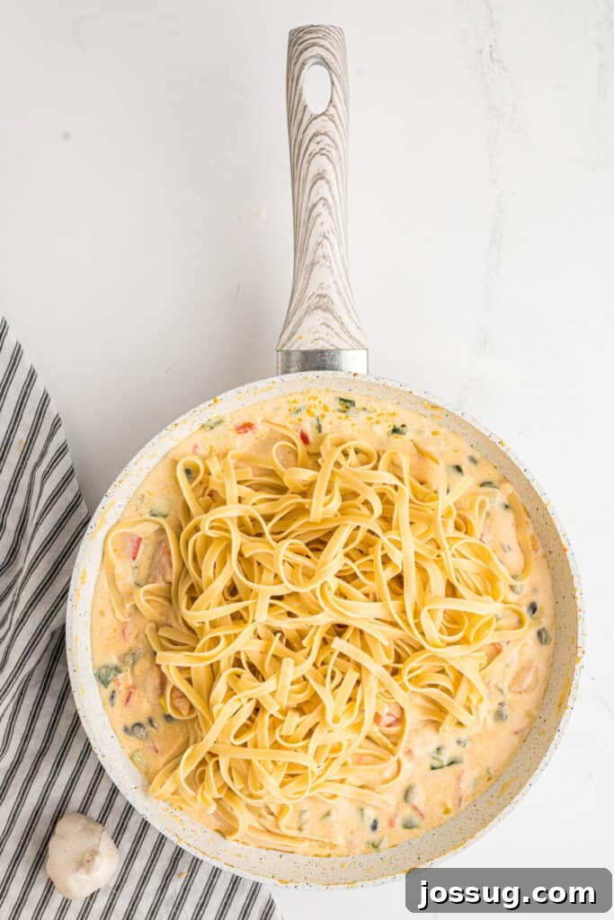 Fiesta Chicken Fettuccine Alfredo 14 Cooked fettuccine noodles gracefully added on top of the southwest alfredo mixture in the skillet, ready to be tossed.