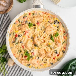 Overhead square crop of skillet filled with Southwest Chicken Fettuccine Alfredo, garnished with parsley.