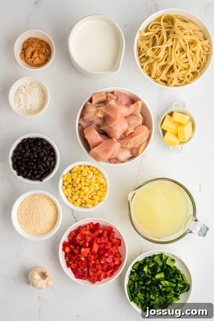 Fiesta Chicken Fettuccine Alfredo 3 Overhead view of fresh ingredients for Southwest Chicken Fettuccine Alfredo, including uncooked fettuccine, diced chicken, bell peppers, black beans, corn, cream, and cheese, arranged on a rustic wooden table.