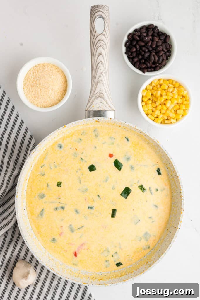 Fiesta Chicken Fettuccine Alfredo 10 A rich, creamy pepper sauce gently simmering in the skillet, with grated parmesan, black beans, and corn waiting to be added.