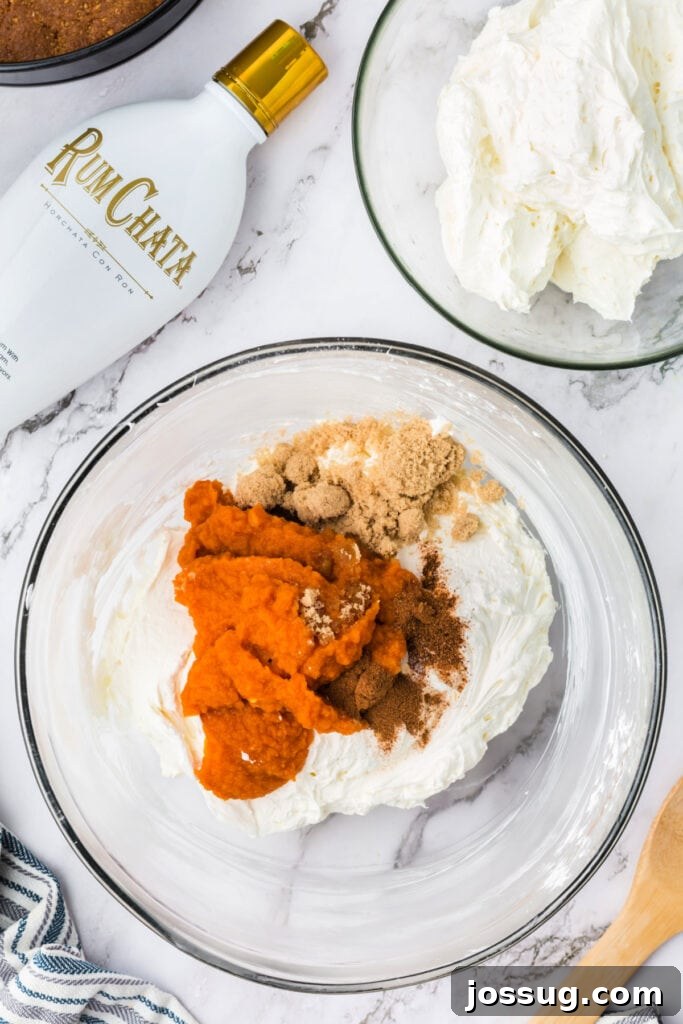 Decadent No-Bake RumChata Pumpkin Cheesecake 12 Cream cheese mixture in a glass bowl with pumpkin puree, brown sugar, and spices added on top, ready to be mixed into the pumpkin cheesecake layer.
