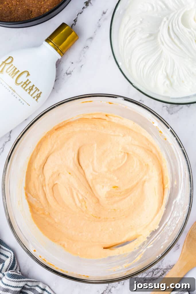 Decadent No-Bake RumChata Pumpkin Cheesecake 13 Bowl of pumpkin cheesecake filling mixed until smooth and creamy, with RumChata bottle, whipped mixture, and springform crust nearby.