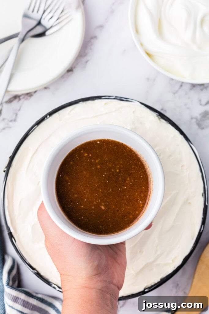 Decadent No-Bake RumChata Pumpkin Cheesecake 17 Hand holding a bowl of prepared cinnamon-brown sugar drizzle topping over the finished layered cheesecake.