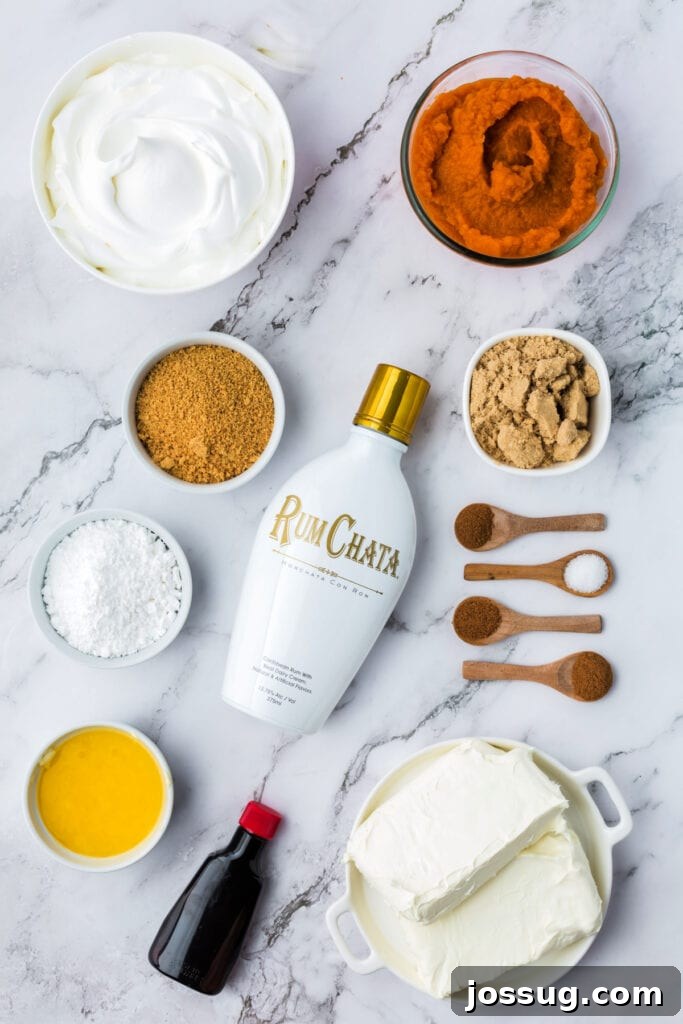 Decadent No-Bake RumChata Pumpkin Cheesecake 3 Overhead view of No Bake RumChata Pumpkin Cheesecake ingredients including cream cheese, pumpkin puree, RumChata bottle, cool whip, sugars, spices, butter, and extract on a marble background.