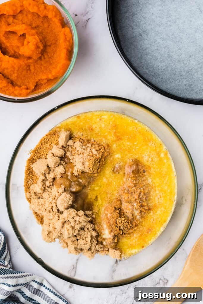 Decadent No-Bake RumChata Pumpkin Cheesecake 4 Mixing bowl filled with graham cracker crumbs, brown sugar, and melted butter for the cheesecake crust, with pumpkin puree and a lined springform pan nearby.