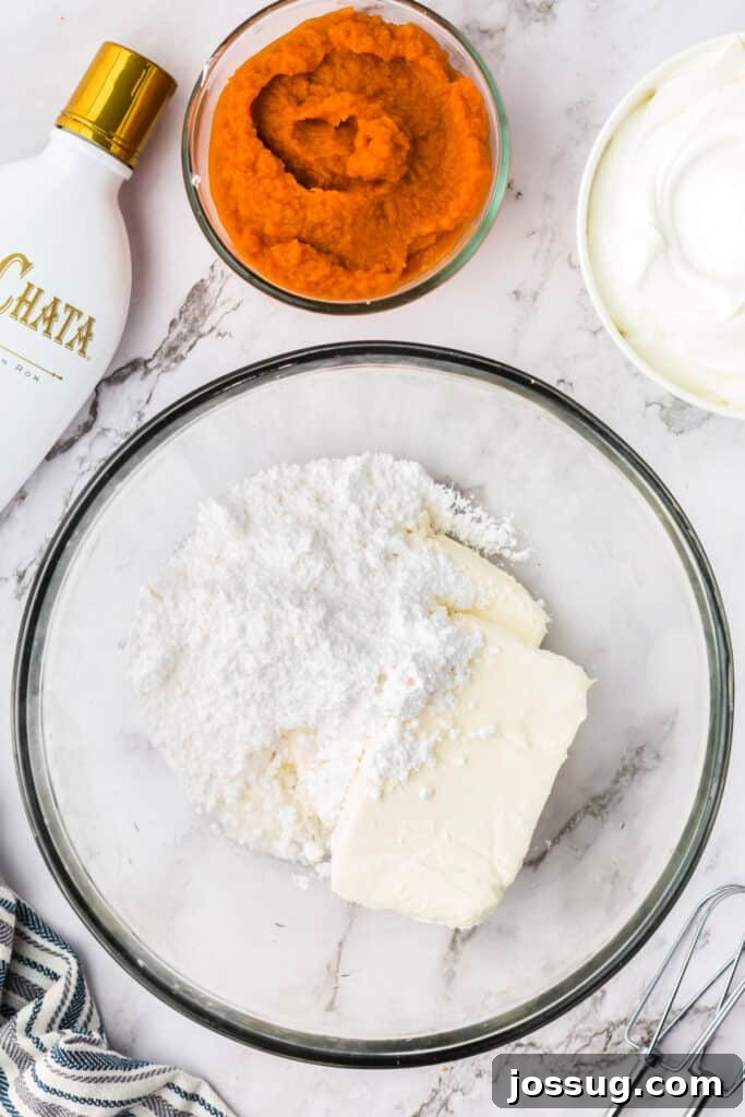 Decadent No-Bake RumChata Pumpkin Cheesecake 8 Mixing bowl with softened cream cheese and powdered sugar before blending, with pumpkin puree and RumChata bottle nearby.