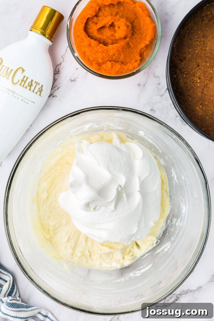 Decadent No-Bake RumChata Pumpkin Cheesecake 10 Bowl of cream cheese mixture topped with a large scoop of cool whip, ready to be folded together for the cheesecake filling.