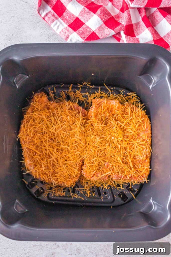 Golden Crispy Air Fried Bone In Pork Chops 12 Two seasoned bone-in pork chops coated with Parmesan and crouton mixture placed in an air fryer basket ready to cook.