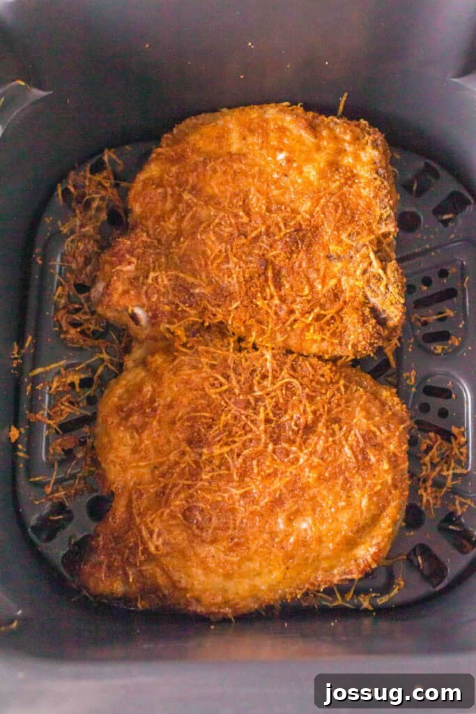 Golden Crispy Air Fried Bone In Pork Chops 13 Two golden brown air fryer bone-in pork chops fresh out of the air fryer basket with crispy Parmesan crust.