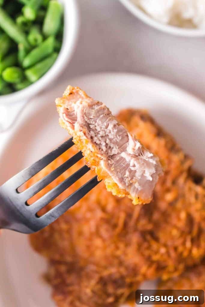Golden Crispy Air Fried Bone In Pork Chops 15 Close-up of a bite of juicy air fryer pork chop on a fork showing tender inside and crispy coating.