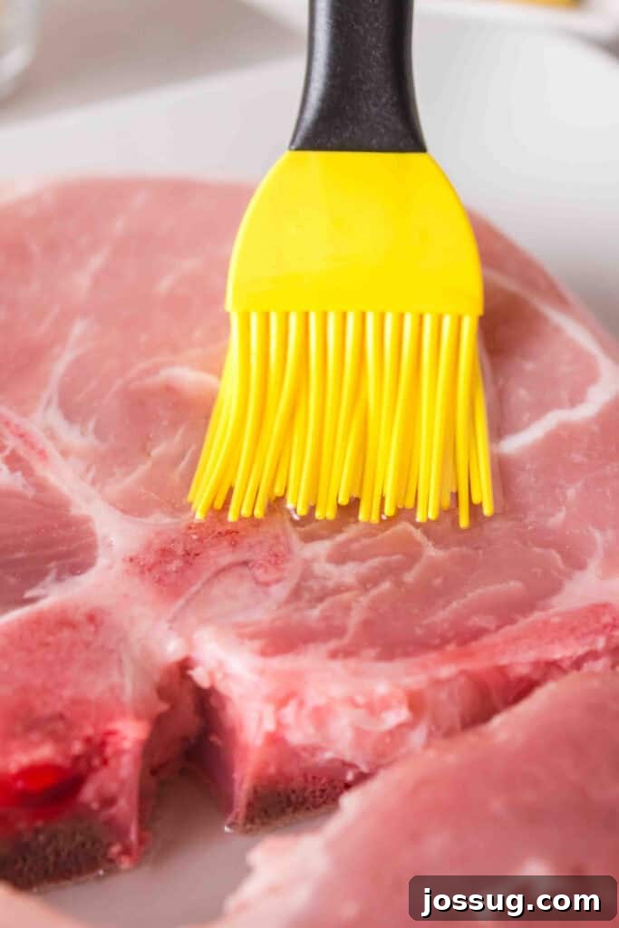Golden Crispy Air Fried Bone In Pork Chops 4 Close-up of raw bone-in pork chop being brushed with olive oil using a yellow silicone brush.