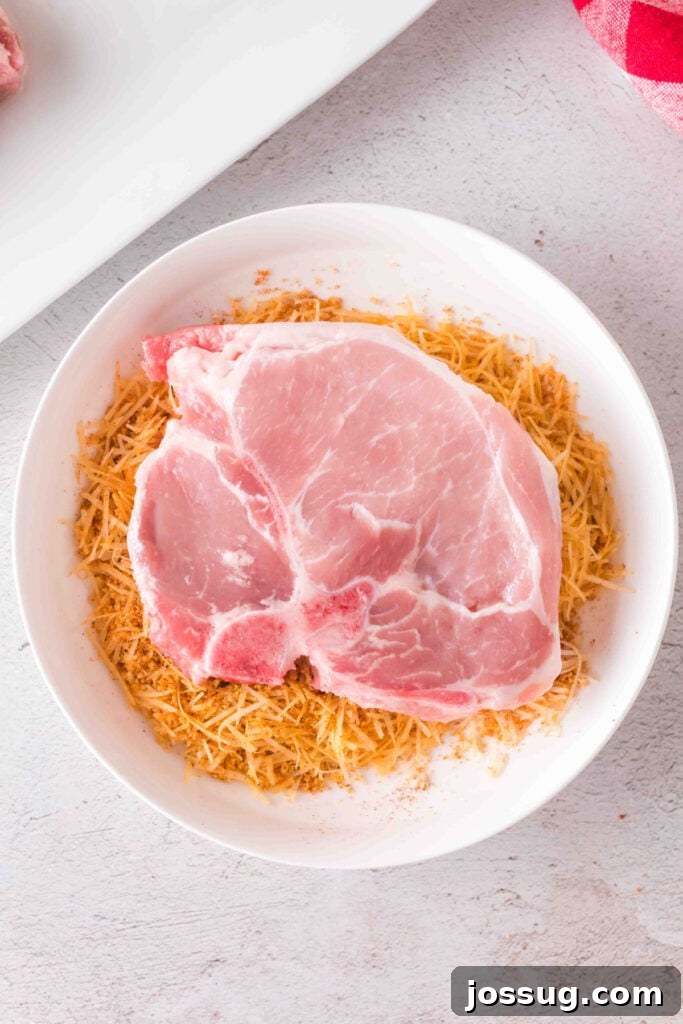 Golden Crispy Air Fried Bone In Pork Chops 10 Raw pork chop placed in a bowl of seasoned Parmesan and crouton mixture before coating.