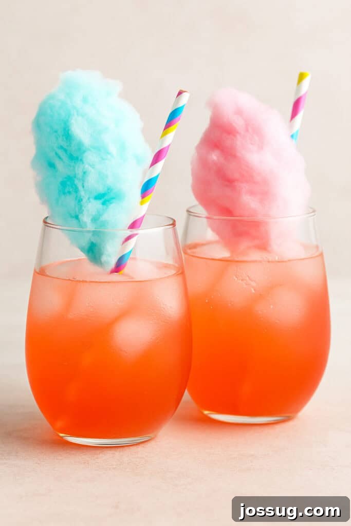 Margarita's Enchanted Circus 2 Two vibrant cotton candy margaritas in stemless glasses, one topped with blue cotton candy and the other with pink, set on a light neutral background with pastel striped straws.