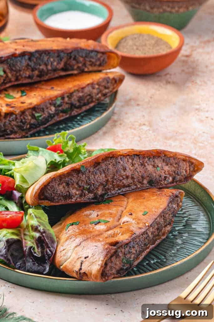 Two arayes halves on a green plate with fresh salad on the side, showing the cooked meat filling inside the crispy pita bread.
