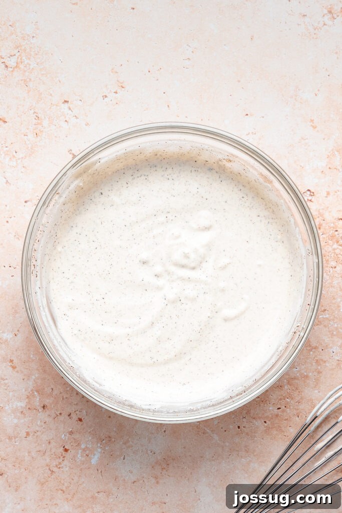 Smooth and creamy shwarma white sauce whisked together in a glass bowl with a whisk nearby.