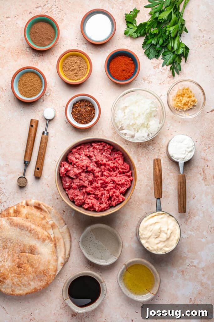 Overhead shot of arayes ingredients including ground beef, ground lamb, spices in small bowls, parsley, pita bread, mayonnaise, yogurt, olive oil, and pomegranate molasses on a light surface.