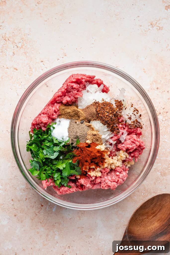 Mixing bowl with ground beef, ground lamb, grated onion, parsley, minced garlic, and spices piled on top, ready to be combined for arayes filling.