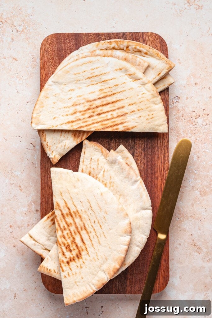 Stack of halved pita bread pieces arranged on a wooden cutting board with a gold knife, ready to be stuffed for arayes.