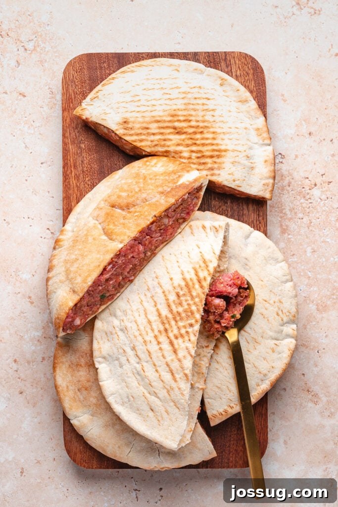 Pita halves stuffed with raw spiced meat mixture arranged on a wooden board with a gold spoon tucked inside one pita showing the filling.