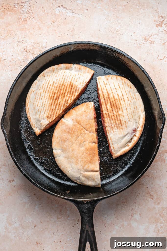 Three raw stuffed pitas cooking in a cast iron skillet, open side down, beginning to sear for arayes.