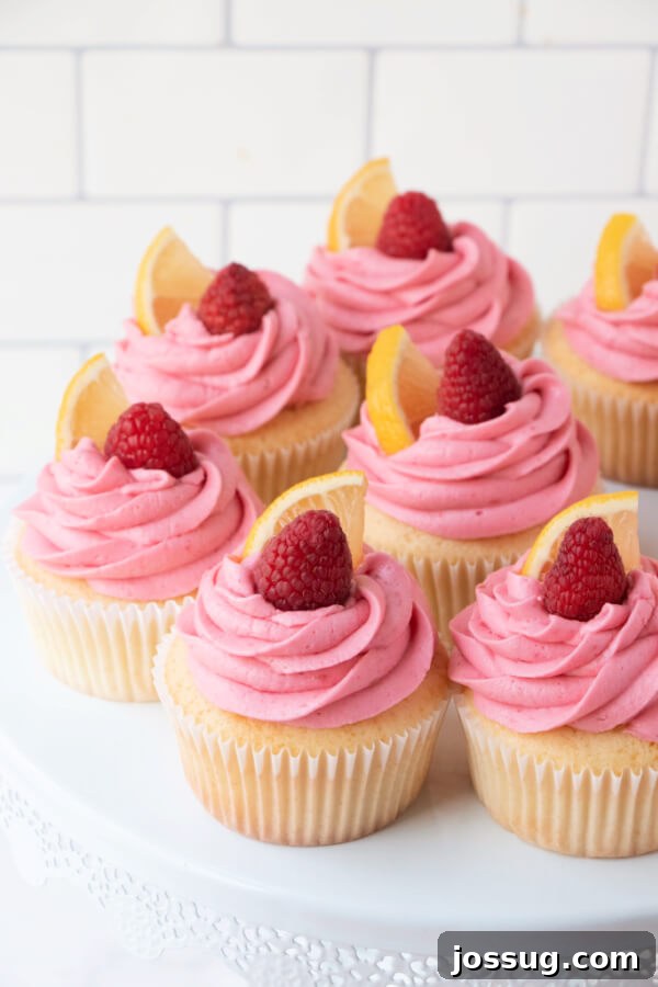 Easy homemade lemon cupcakes with vibrant raspberry buttercream frosting presented on a white cake stand