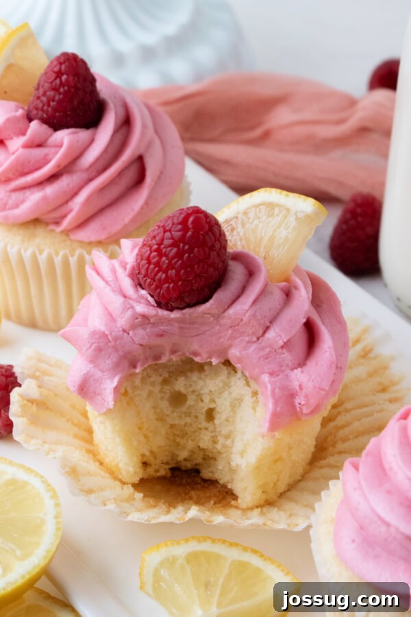 A frosted lemon and raspberry cupcake with a bite taken out, revealing the moist cake texture