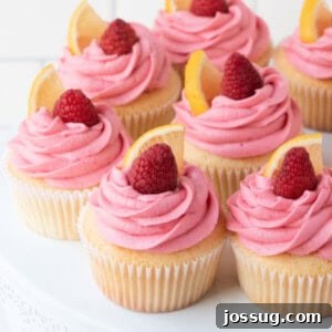Closeup of lemon cupcakes with raspberry buttercream frosting on a white cake stand, showcasing the vibrant colors and appealing texture