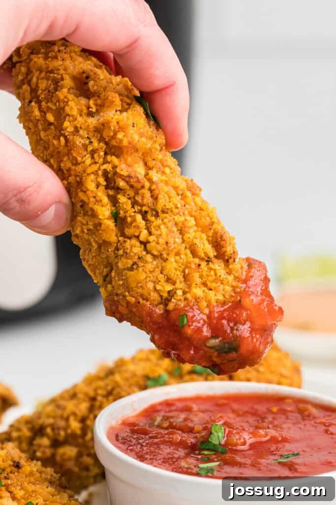 Hand dipping a golden-brown crispy southwest chicken tender into a vibrant bowl of salsa, highlighting its crunchy exterior.