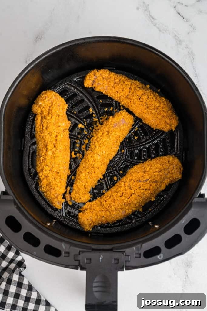 Breaded chicken tenders neatly arranged in a single layer in the air fryer basket before cooking to ensure even crisping.