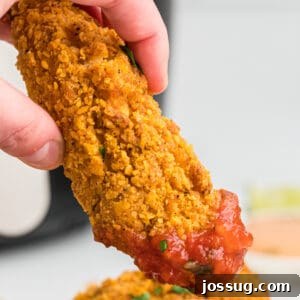 Close-up square photo of a hand dipping a golden-brown southwest chicken tender into a vibrant bowl of salsa.