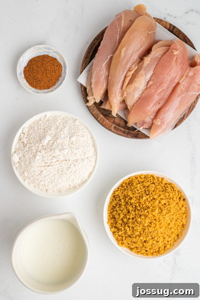 Ingredients for crispy southwest chicken tenders including raw chicken tenderloins, a bowl of crushed corn chips, flour, buttermilk, and chili powder ready for preparation.