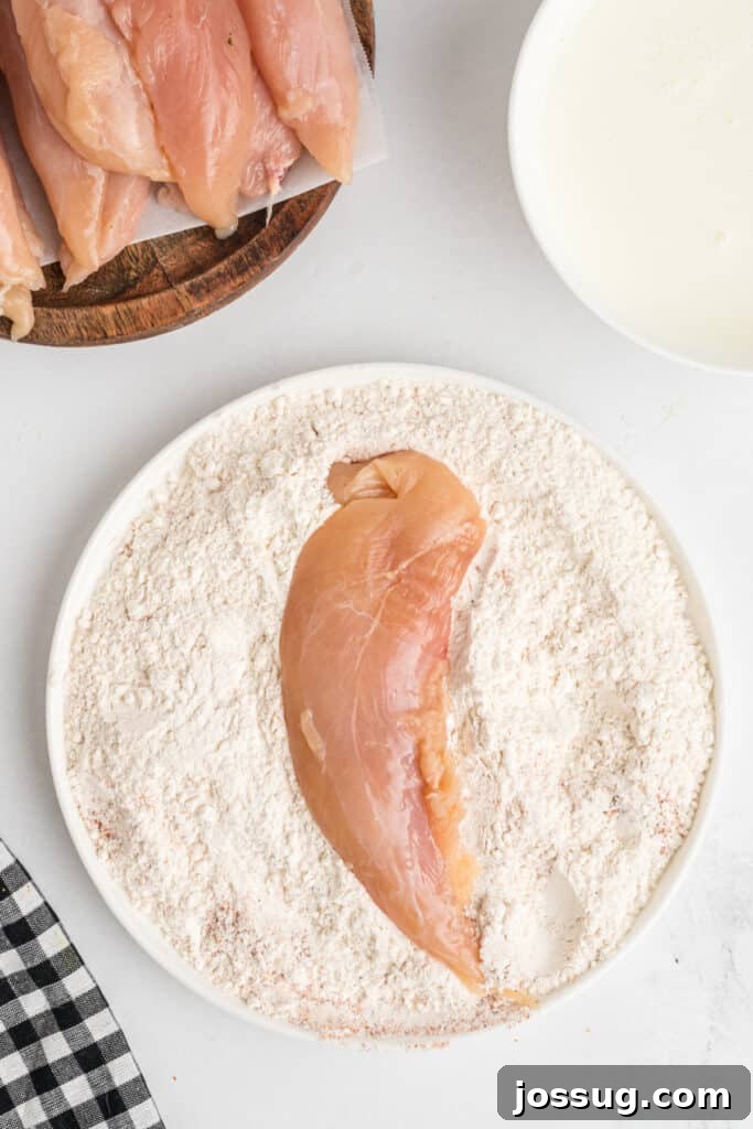 Raw chicken tenderloin being carefully dredged in seasoned flour for southwest chicken tenders, ensuring an even coat.