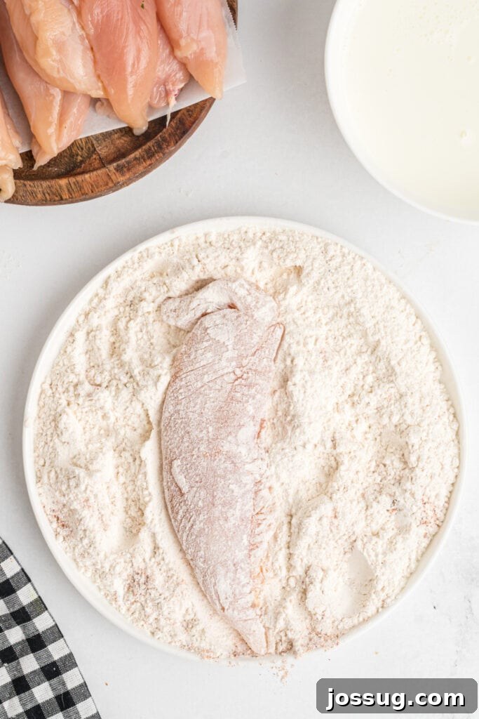 Raw chicken tenderloin fully coated in seasoned flour mixture, ready for the next dipping step in buttermilk.