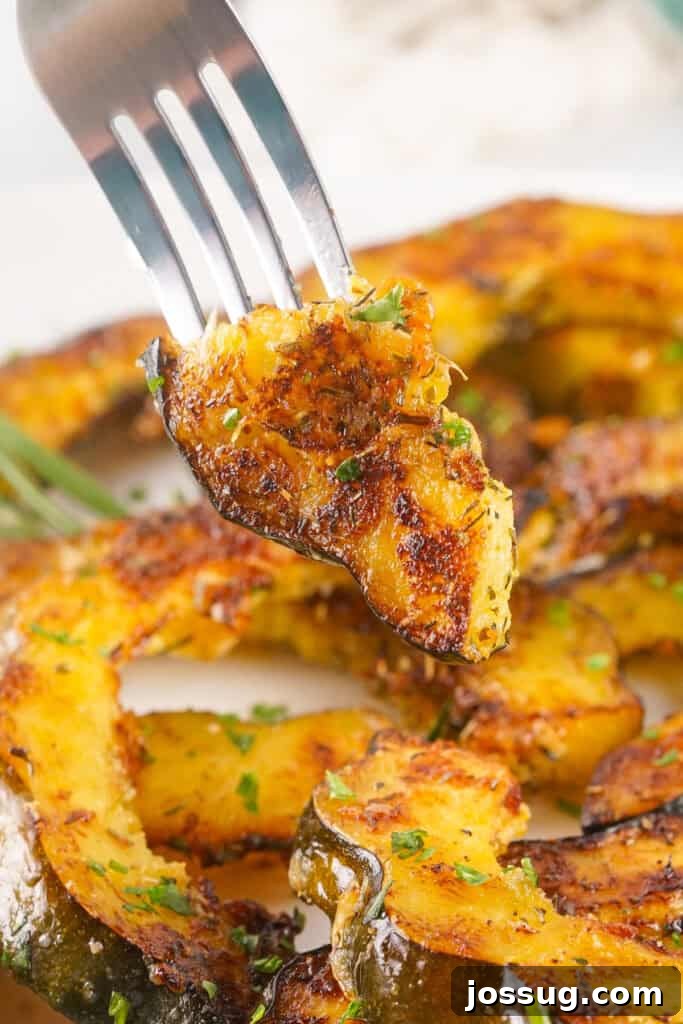 Caramelized Acorn Squash 12 Close-up of a fork holding a bite of roasted acorn squash topped with herbs and parmesan.
