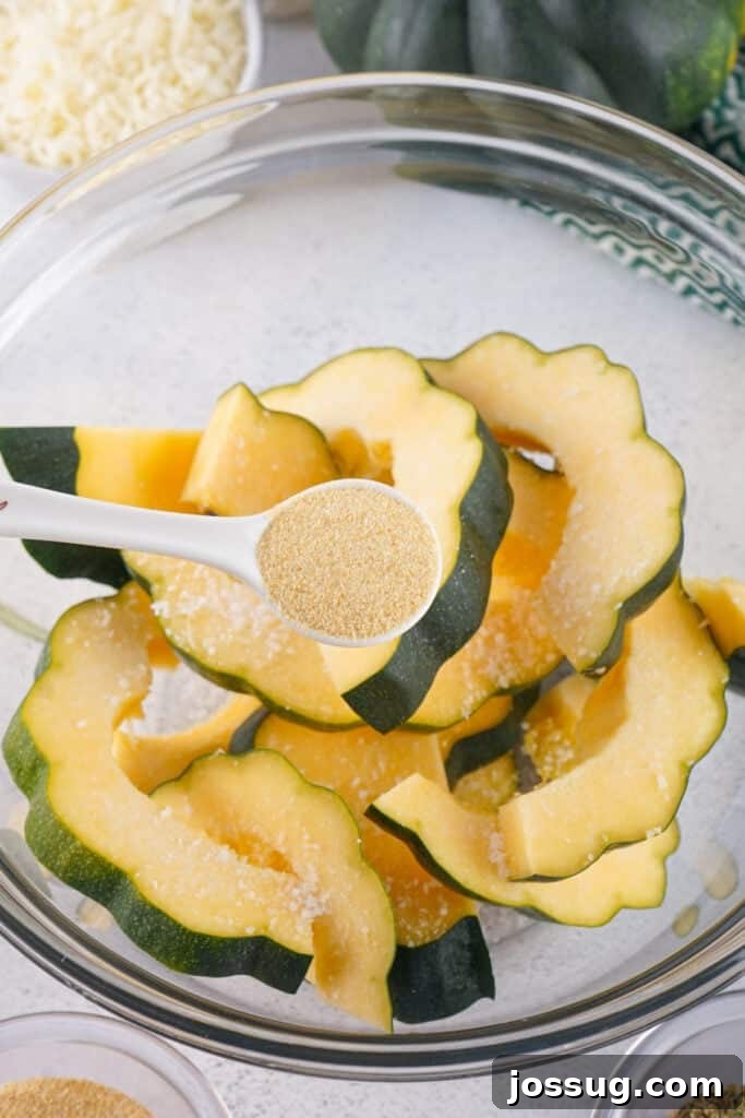 Caramelized Acorn Squash 5 Spoonful of garlic powder being sprinkled over acorn squash slices in a mixing bowl.