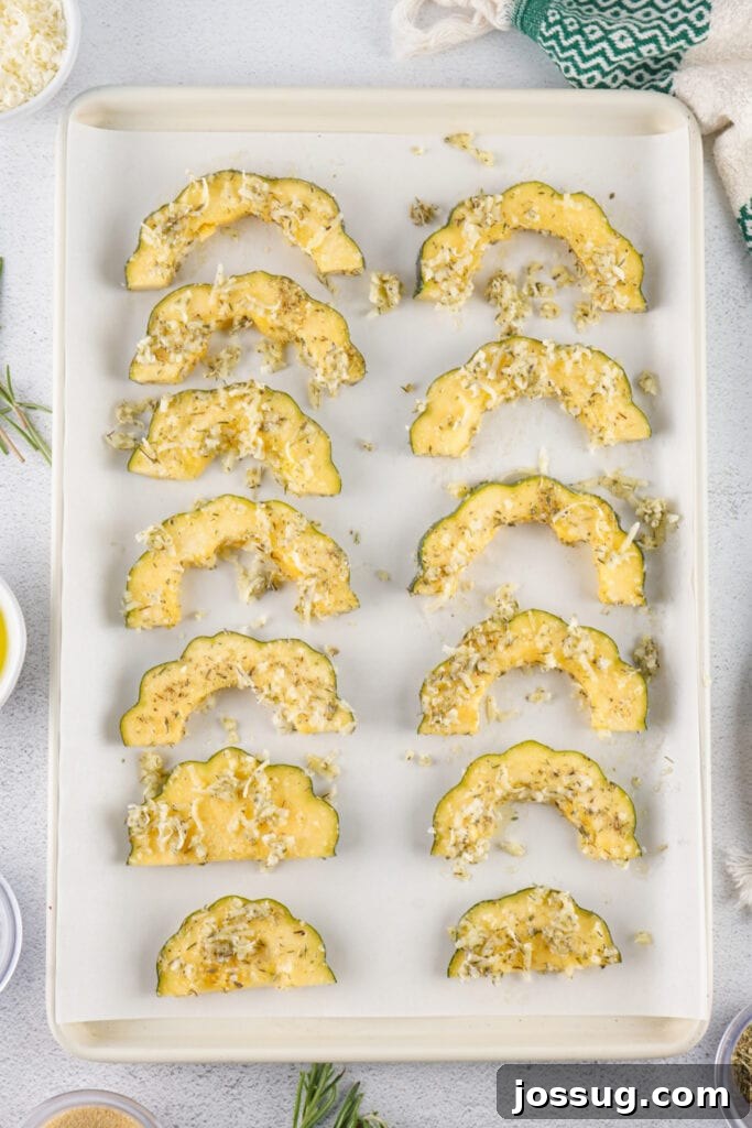 Caramelized Acorn Squash 10 Uncooked acorn squash slices on a parchment-lined baking sheet topped with parmesan and herbs.