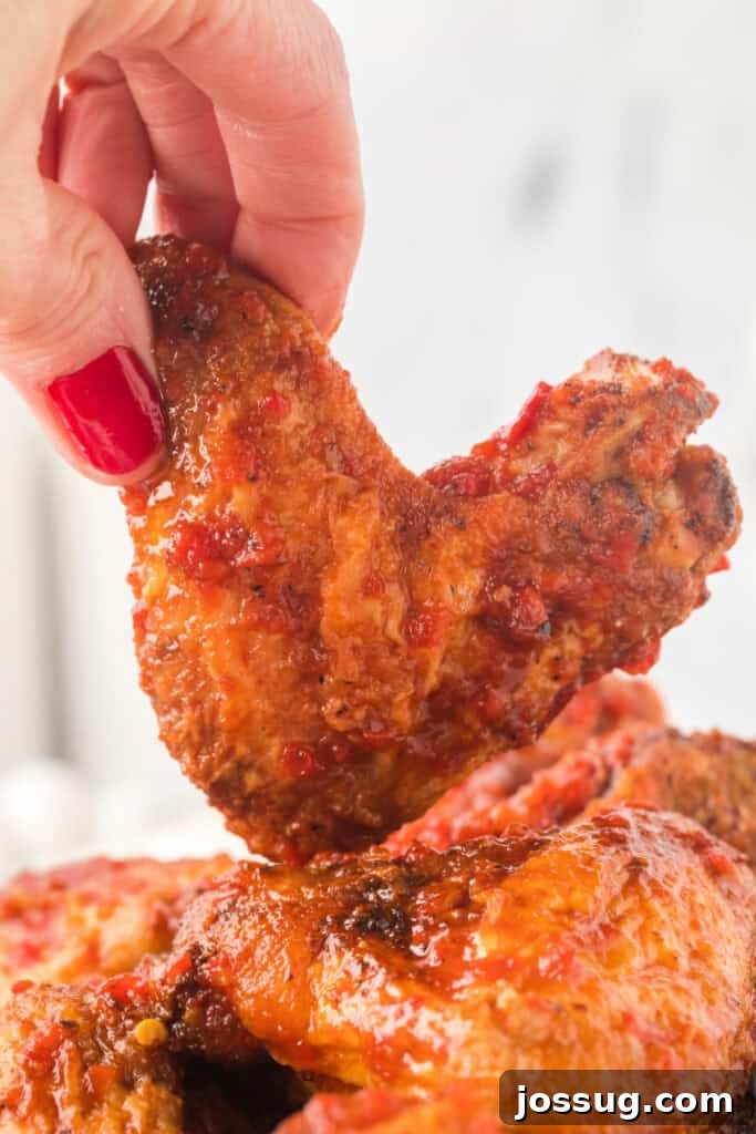 Smoky Sweet Air Fryer Chipotle Honey Glazed Wings 2 Close-up of a hand holding a saucy chipotle honey chicken wing with red nail polish.