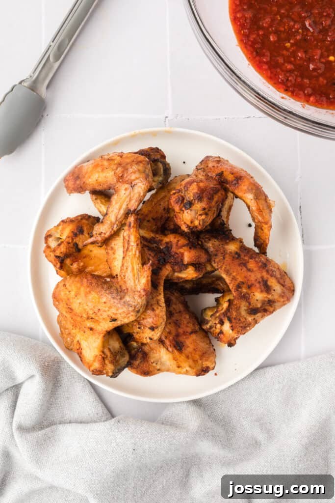 Smoky Sweet Air Fryer Chipotle Honey Glazed Wings 12 Crispy golden brown cooked chicken wings on a white plate with a bowl of chipotle honey sauce beside them.