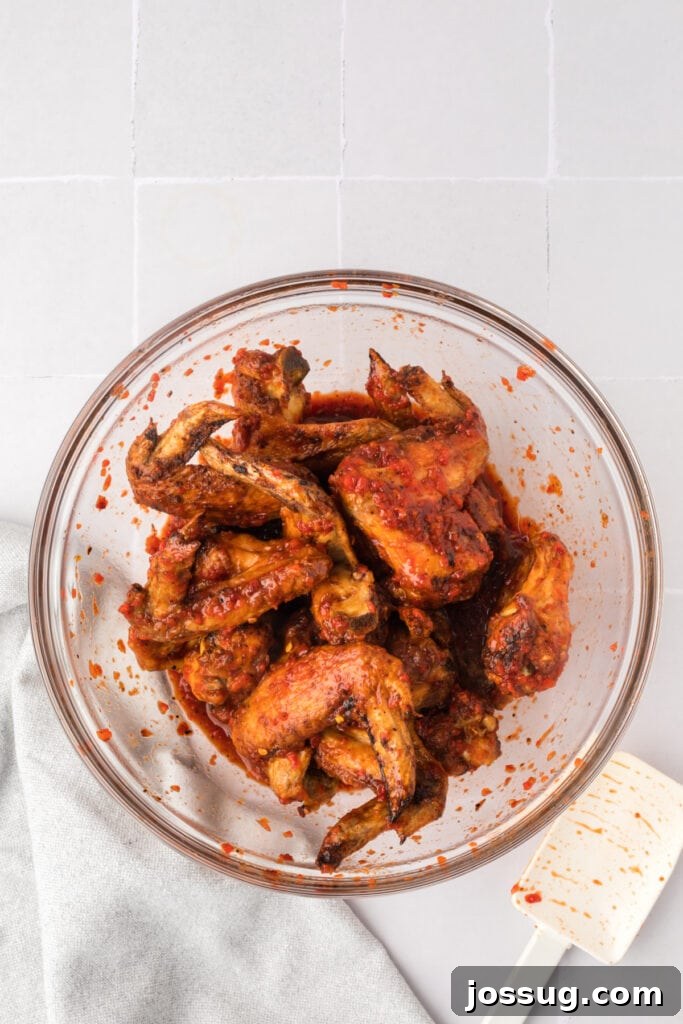 Smoky Sweet Air Fryer Chipotle Honey Glazed Wings 13 Cooked chicken wings tossed in chipotle honey sauce inside a glass bowl with a white spatula resting nearby.