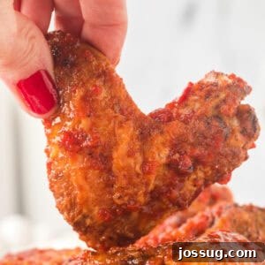 Hand holding a crispy chipotle honey wing close up, highlighting the saucy coating and charred edges.