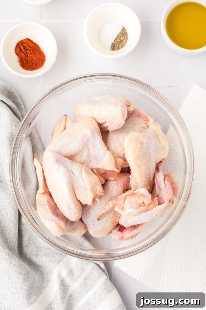 Smoky Sweet Air Fryer Chipotle Honey Glazed Wings 5 Close-up of raw chicken wings in a glass bowl with seasoning bowls nearby on a white tile counter with a striped kitchen towel.