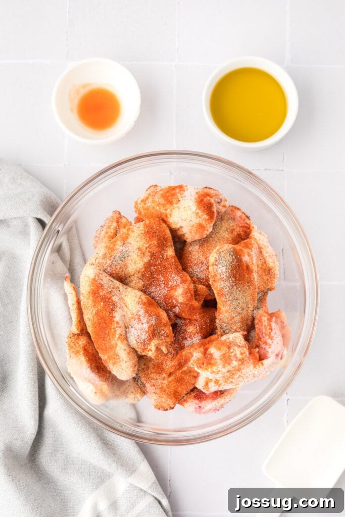 Smoky Sweet Air Fryer Chipotle Honey Glazed Wings 6 Raw chicken wings coated with garlic powder, paprika, salt, and pepper in a glass bowl with oil and hot sauce bowls beside it.