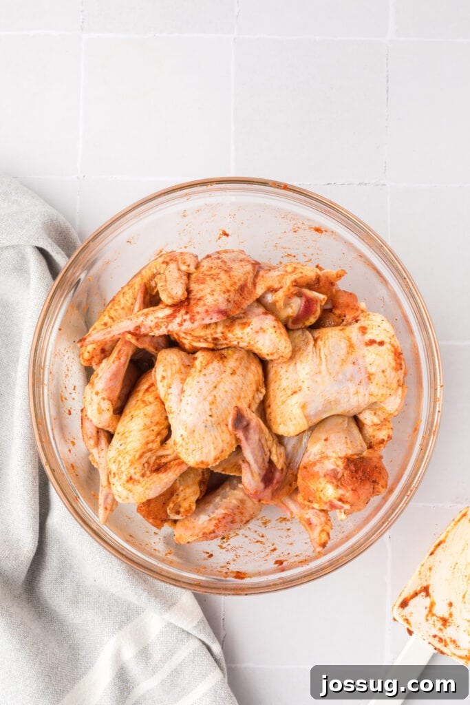 Smoky Sweet Air Fryer Chipotle Honey Glazed Wings 7 Chicken wings tossed with seasoning and hot sauce in a glass bowl with a spatula resting on the side.