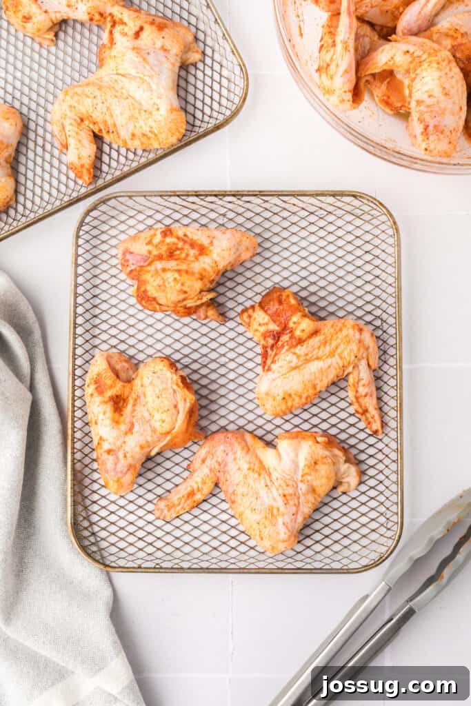 Smoky Sweet Air Fryer Chipotle Honey Glazed Wings 8 Raw seasoned chicken wings arranged on an air fryer rack with tongs and a mixing bowl in the background.