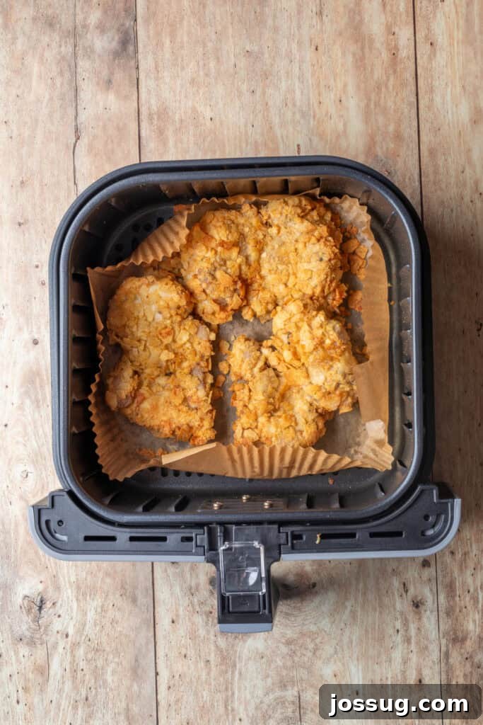 Cowboy Butter Chicken Crunch Sandwich 9 Crispy potato chip-coated chicken thighs air frying in a basket lined with parchment paper, showing the golden-brown and crunchy texture developing.
